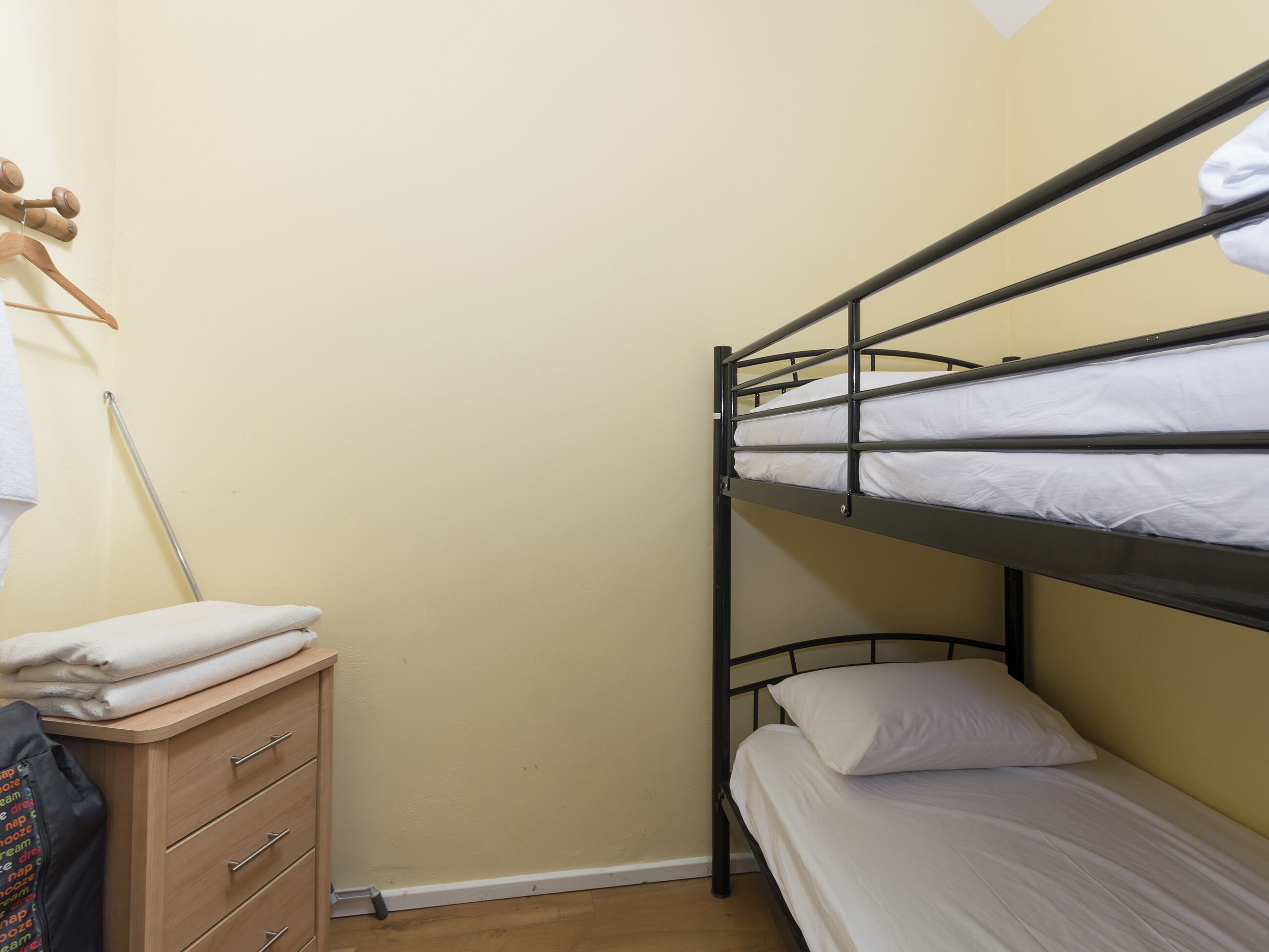A bunk bed room with a wooden dresser and a hanging towel rack.