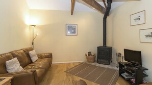 Ein Wohnzimmer mit braunem Ledersofa, Fernseher, Kamin und Holzbalken an der Decke.