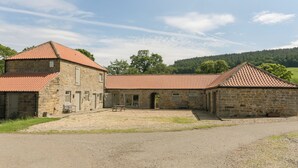 Ein Steinhaus mit rotem Ziegeldach, einem Schotterweg und einer Rasenfläche.