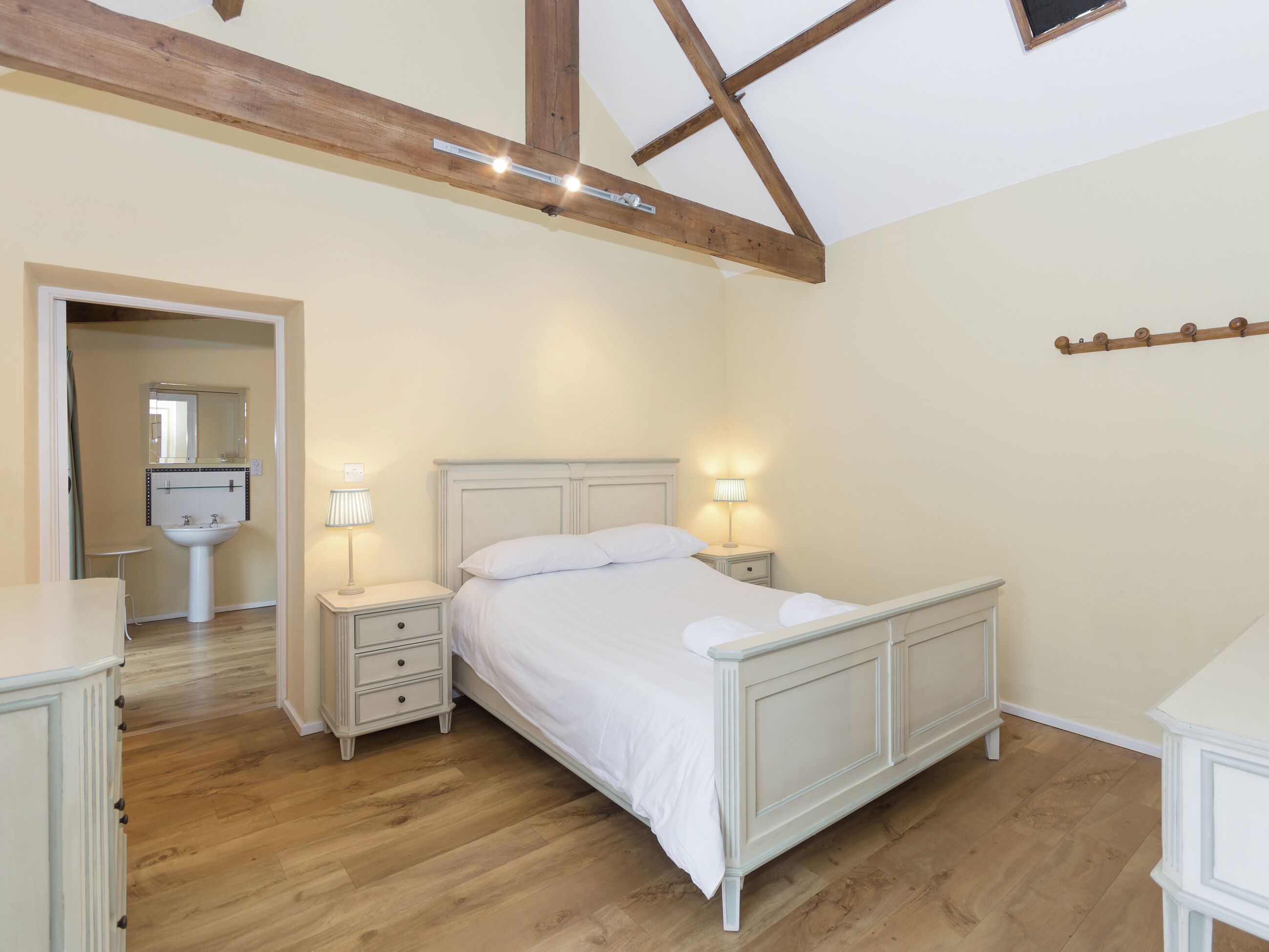 Une chambre à coucher avec un lit, des tables de chevet, un miroir et un lavabo.