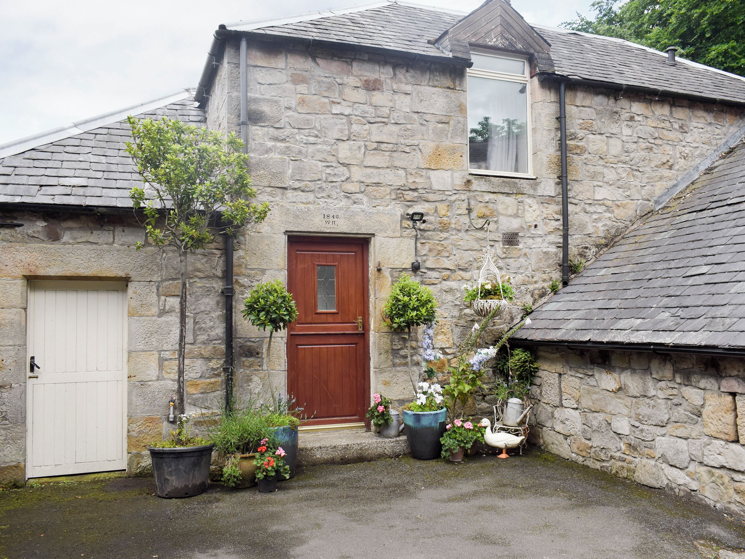 A stone building with a wooden door, a window, and various potted plants.
