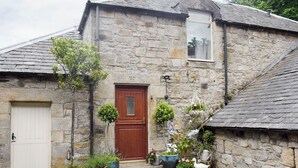 A stone building with a wooden door, a window, and various potted plants. - Kielder Cottage Spa - E3533 (Kielder)