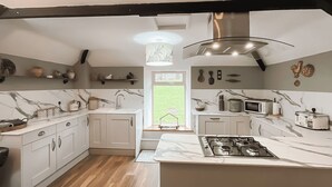 A modern kitchen with white cabinetry, a central island with a stove, and a window providing a view of the outdoors. - Kielder Cottage Spa - E3533 (Kielder)
