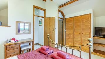 Una camera da letto con un letto, un'armadietto in legno, una scrivania con una sedia, una televisione e una finestra.