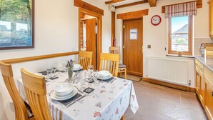 Zona pranzo con tavolo in legno apparecchiato per quattro, una sedia di legno, un orologio appeso al muro e una finestra con vista sull'esterno.