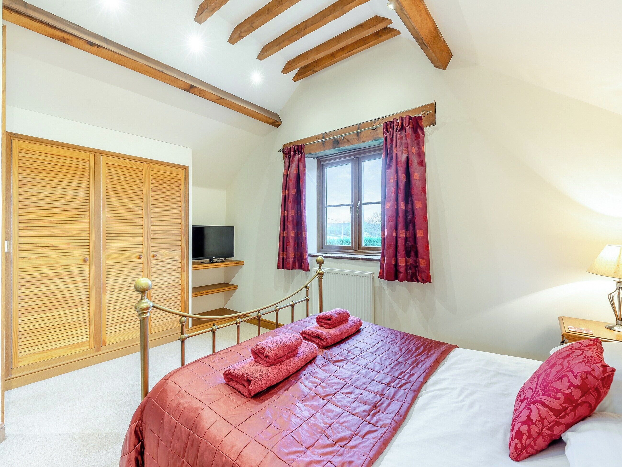 Quarto com cama, televisão, janela com cortinas e teto de madeira.