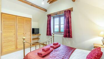 Quarto com cama, televisão, janela com cortinas e teto de madeira.