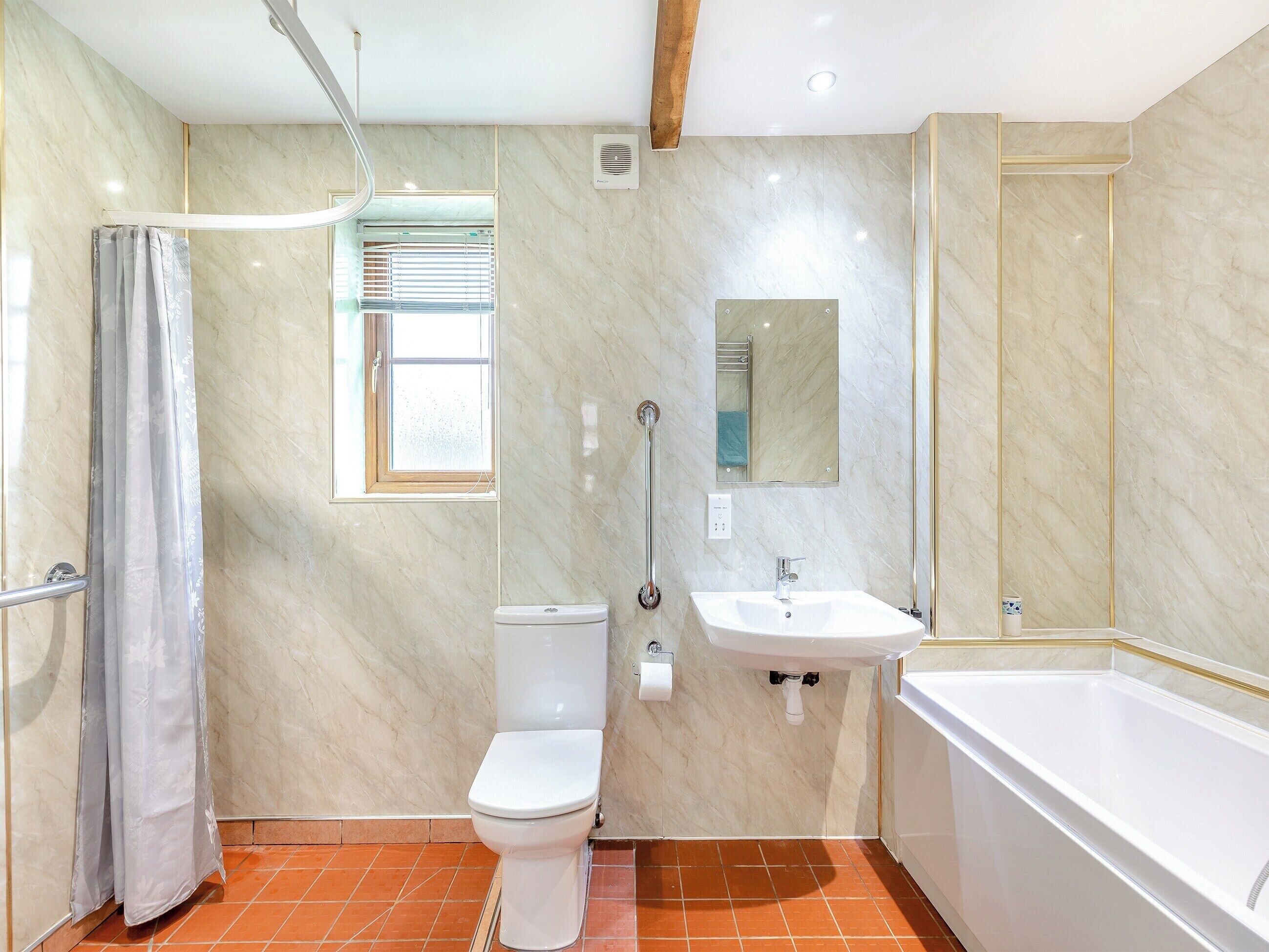 Un baño con inodoro, lavamanos, bañera, ducha y una ventana con persianas.