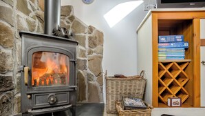 A wood-burning stove with a fire, a wicker basket, and a bookshelf with books. - 1 bedroom accommodation in Tealing, near Dundee (Tealing, near Dundee)