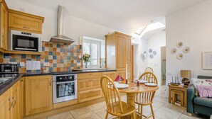 A compact kitchen with wooden cabinets, a microwave, an oven, and a dining area with a table and chairs. - 1 bedroom accommodation in Tealing, near Dundee (Tealing, near Dundee)
