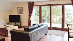 A living room with a sofa, a television, and a balcony with a view of greenery. - 3 bedroom accommodation in Oakley, near Dunfermline (Oakley, near Dunfermline)