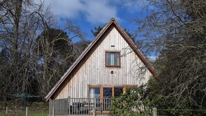 A wooden cabin with a balcony, surrounded by trees and a fence. - 3 bedroom accommodation in Oakley, near Dunfermline (Oakley, near Dunfermline)