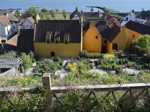 A yellow building with a tiled roof, surrounded by greenery and a body of water in the background. - 3 bedroom accommodation in Oakley, near Dunfermline (Oakley, near Dunfermline)