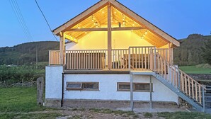 Une cabane en bois à deux étages, dotée d’un balcon, d’un escalier et offrant une vue sur une colline boisée.