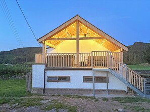 A two-story wooden cabin with a balcony, a staircase, and a view of a forested hillside. - 3 bedroom accommodation in Blawith, near Coniston (Blawith, near Coniston)
