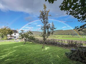 A house with a stone wall and a tree in the foreground, a grassy field, and a mountain range in the background. - 3 bedroom accommodation in Blawith, near Coniston (Blawith, near Coniston)