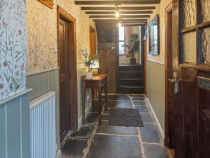 A narrow hallway with patterned wallpaper, a wooden door, a staircase, and a potted plant. - 3 bedroom accommodation in Blawith, near Coniston (Blawith, near Coniston)