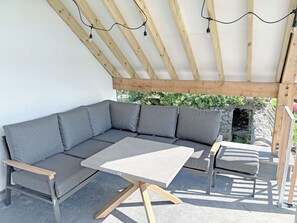 An outdoor seating area with a grey sectional sofa, a small table, and a wooden bench. - 3 bedroom accommodation in Blawith, near Coniston (Blawith, near Coniston)