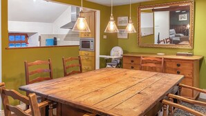 Un coin repas avec une table et des chaises en bois, une cuisine à l’arrière-plan et un miroir au mur.