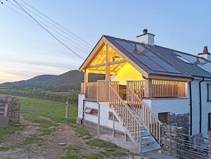 A house with a wooden balcony, a staircase, and a view of the countryside.