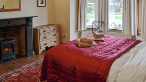 A bedroom with a fireplace, a bed with a red quilt, a dresser, and a window with curtains. - 5 bedroom accommodation in Happisburgh (Happisburgh)
