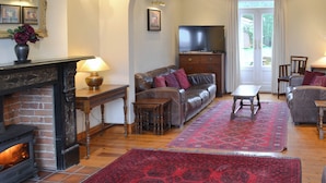 A living room with a fireplace, leather sofas, a television, and a red patterned rug. - 5 bedroom accommodation in Happisburgh (Happisburgh)