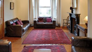 A living room with a brown leather sofa, a wooden coffee table, and a red patterned rug. - 5 bedroom accommodation in Happisburgh (Happisburgh)