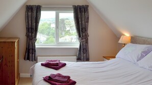Quarto com cama, mesa de cabeceira, luminária e vista para uma cidade pela janela.
