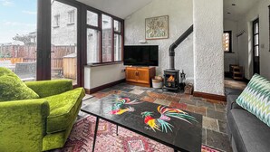 Un salón amplio con un gran ventanal, chimenea, televisor y sillones verdes.