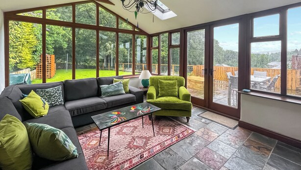 Un salón amplio con un gran ventanal, un sofá, un sillón verde y una alfombra estampada.