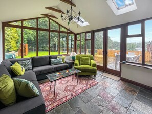 Un salon spacieux avec une grande fenêtre, un canapé, un fauteuil vert et un tapis à motifs.