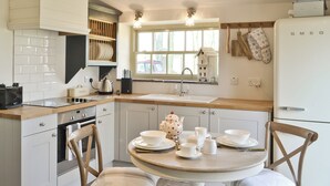 Una cocina moderna con armarios blancos, encimera de madera, una mesa redonda con sillas y un horno empotrado.