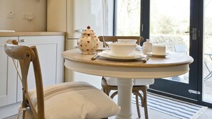 Una cocina con un refrigerador blanco, sillas de madera, una mesa redonda con mantel blanco y una ventana que da a unas vistas de árboles.