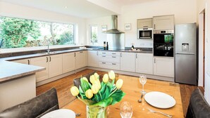 A modern kitchen with a dining area, featuring a large window, stainless steel appliances, and a wooden dining table set for two.