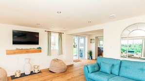 A spacious living room with a blue sofa, wooden flooring, a flat-screen TV, and a view of the outdoors.