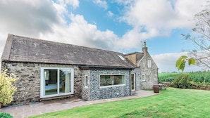 A stone house with a sloped roof, a large window, and a well-maintained lawn.