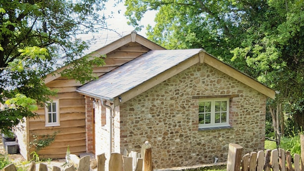 A rustic stone cabin with a wooden exterior, a pitched roof, and a small window.