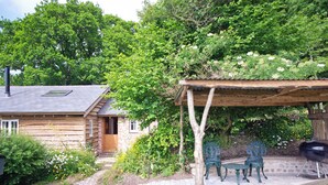 A rustic cabin with a wooden deck, a covered outdoor seating area, and a barbecue grill.