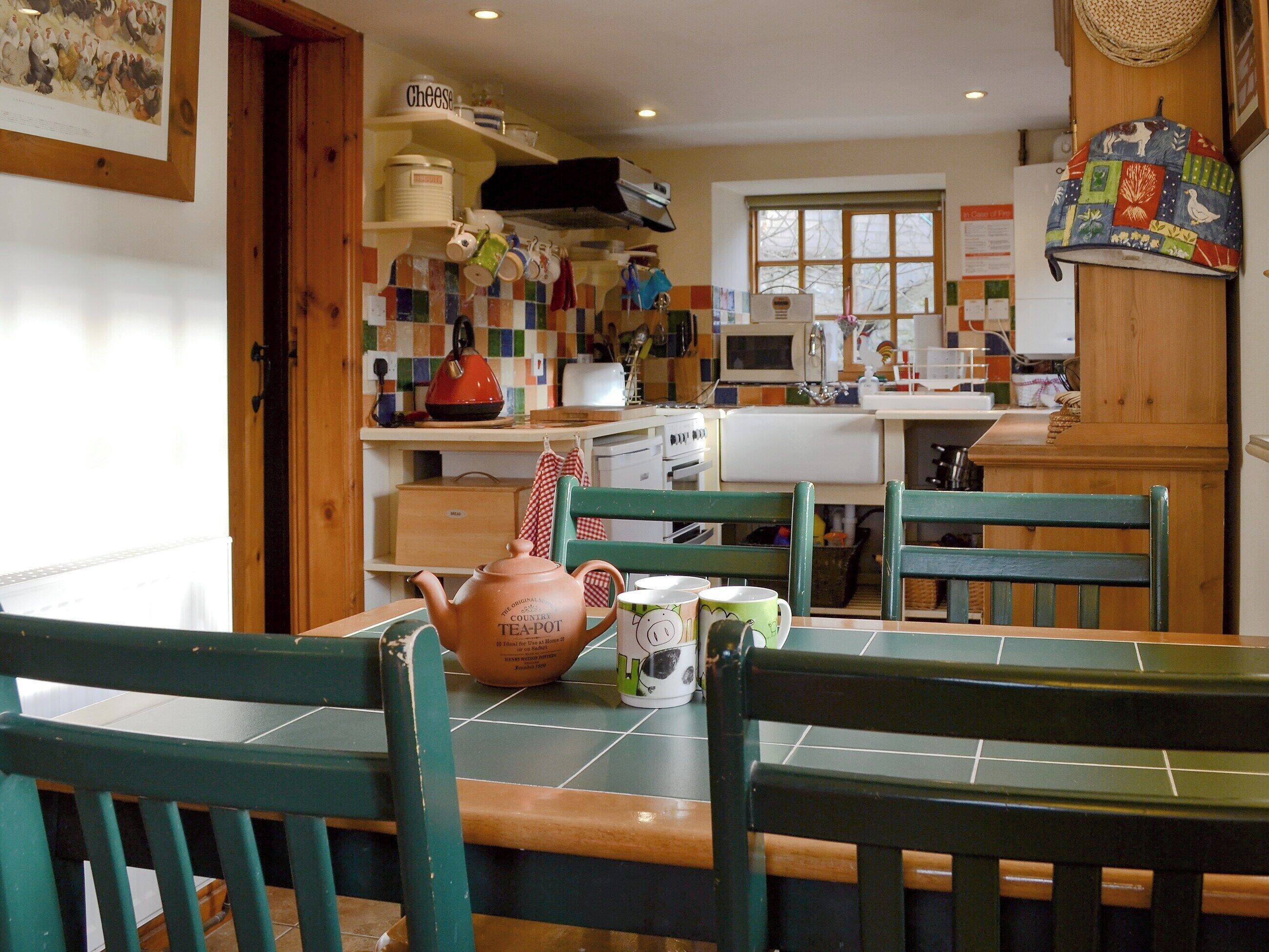 A kitchen with wooden cabinets, a tea pot, and a window.