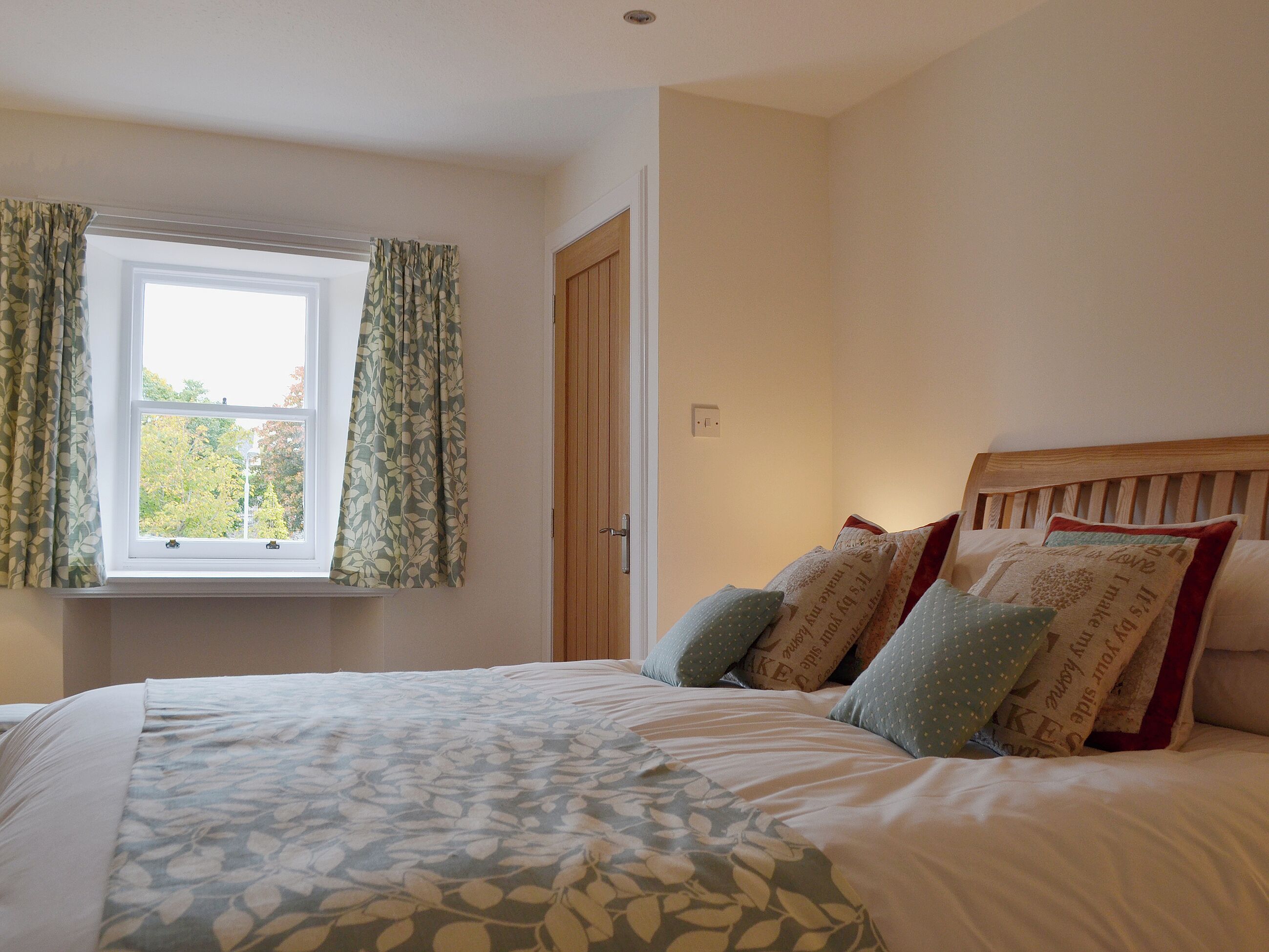 Une chambre à coucher avec un lit, une couvre-lit à motifs floraux, une fenêtre avec des rideaux et une porte en bois.