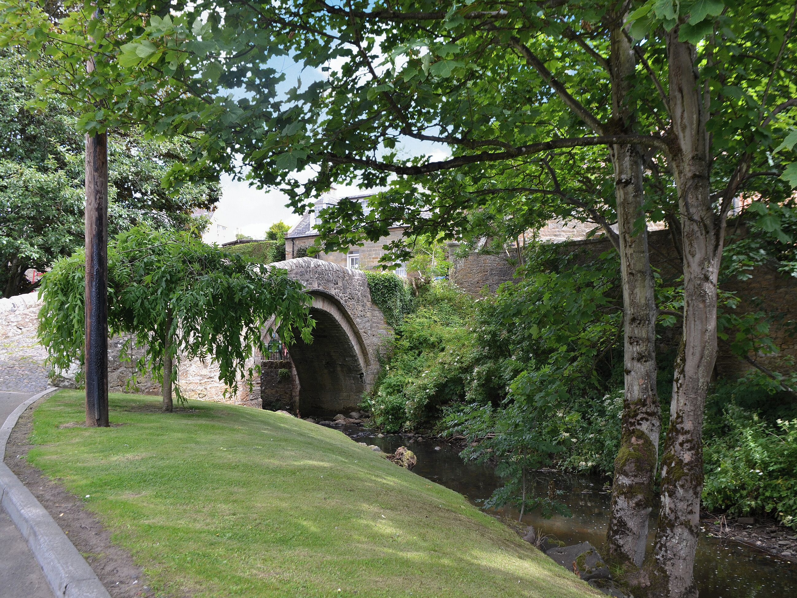 A stone bridge over a stream, surrounded by lush greenery and trees.