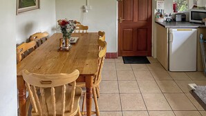 A dining area with a wooden table and chairs, a vase with flowers, and a kitchen with a microwave and toaster. - 2 bedroom accommodation in Shaftesbury (Shaftesbury)