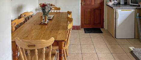 A dining area with a wooden table and chairs, a vase with flowers, and a kitchen with a microwave and toaster.
