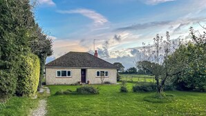 A single-story house with a paved driveway leading to the front door, surrounded by a well-maintained lawn and a variety of shrubs and small trees. - 2 bedroom accommodation in Shaftesbury (Shaftesbury)