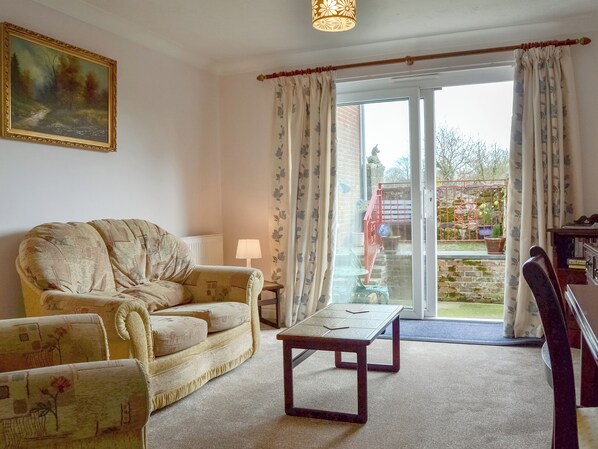 A living room with a sofa, a table, and a lamp. There is a painting on the wall and a view of the outside through a glass door. - 1 bedroom accommodation in Apse Heath, near Shanklin (Apse Heath, near Shanklin)