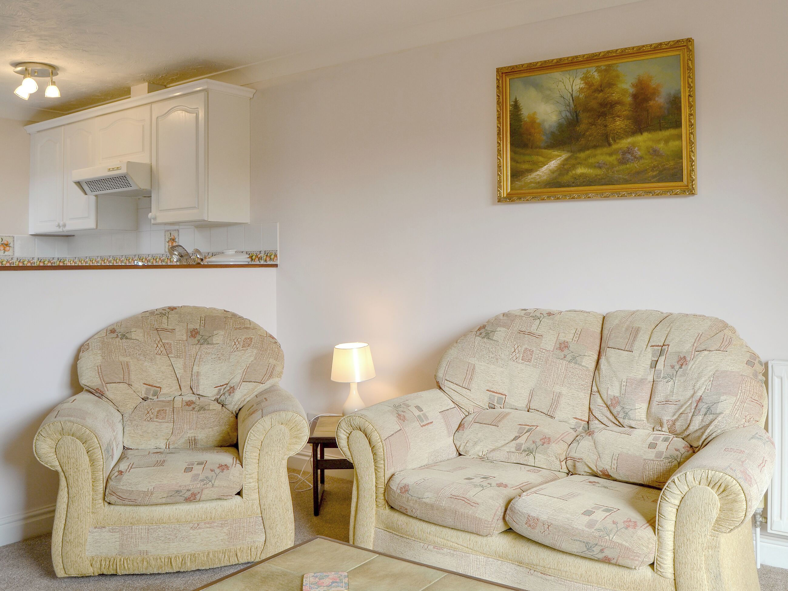 A living room with two armchairs, a small table, and a painting on the wall.