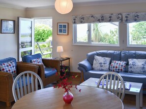 A cozy living room with wicker furniture, a blue sofa, and a dining table with a vase of flowers. - 2 bedroom accommodation in St Merryn, near Padstow (St Merryn, near Padstow)