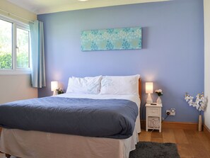 A bedroom with a bed, bedside lamps, a wall-mounted artwork, and a window with curtains.