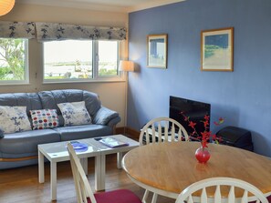 A living room with a sofa, a small table, a wooden dining table, chairs, a TV, and two framed pictures on the wall.