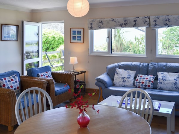 A cozy living room with wicker furniture, a blue sofa, and a dining table with a vase of flowers. - 2 bedroom accommodation in St Merryn, near Padstow (St Merryn, near Padstow)